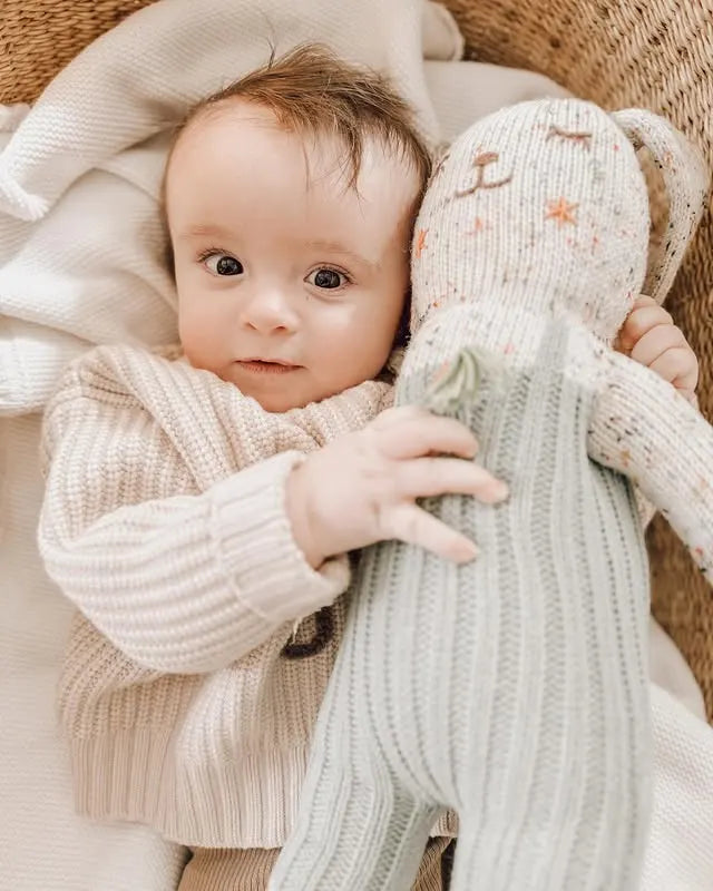 Baby holding a knitted toy with a soft blanket in the background