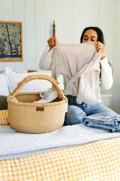 Woman folding laundry on a bed with a woven basket nearby