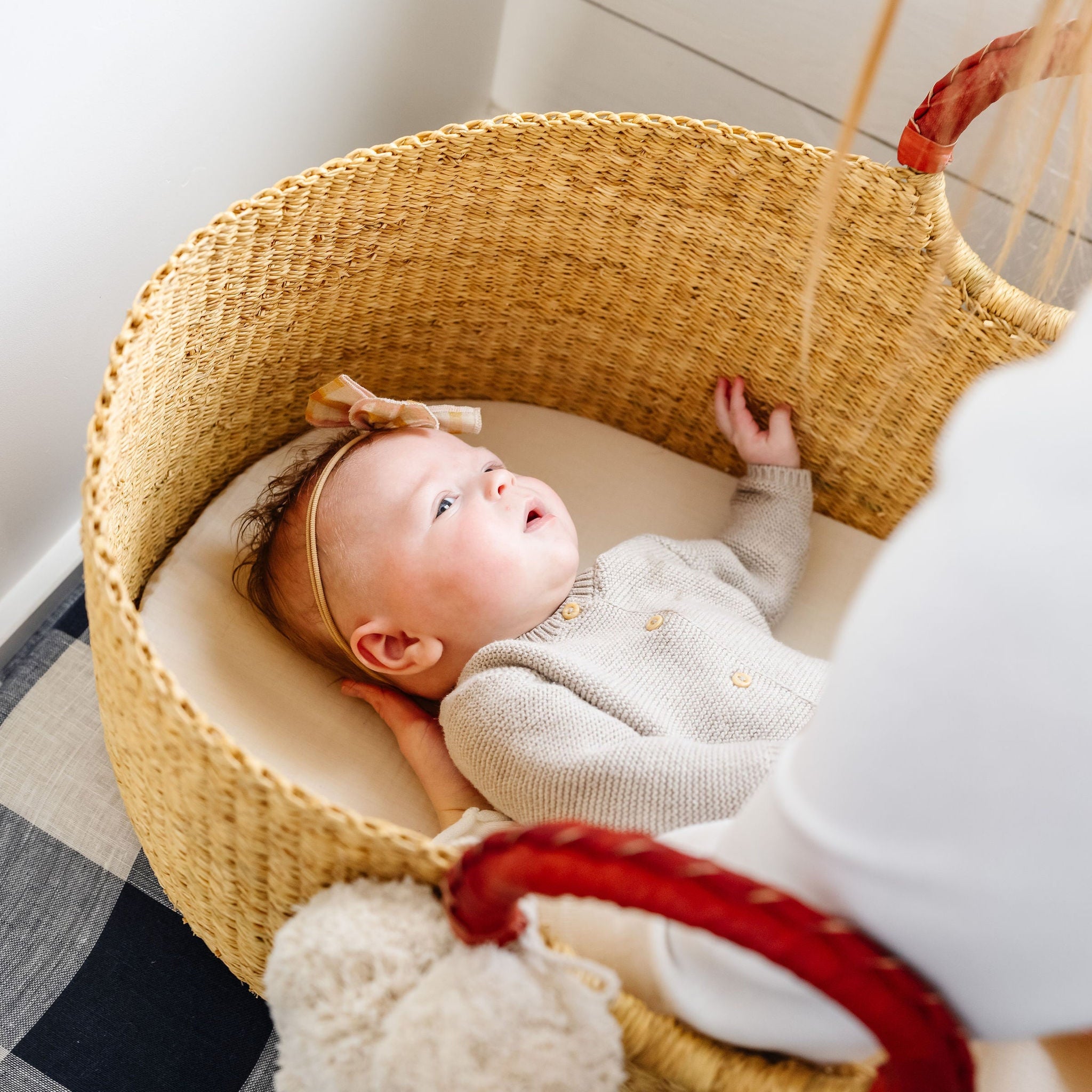 Baby lying in a woven bassinet with a checkered blanket underneath
