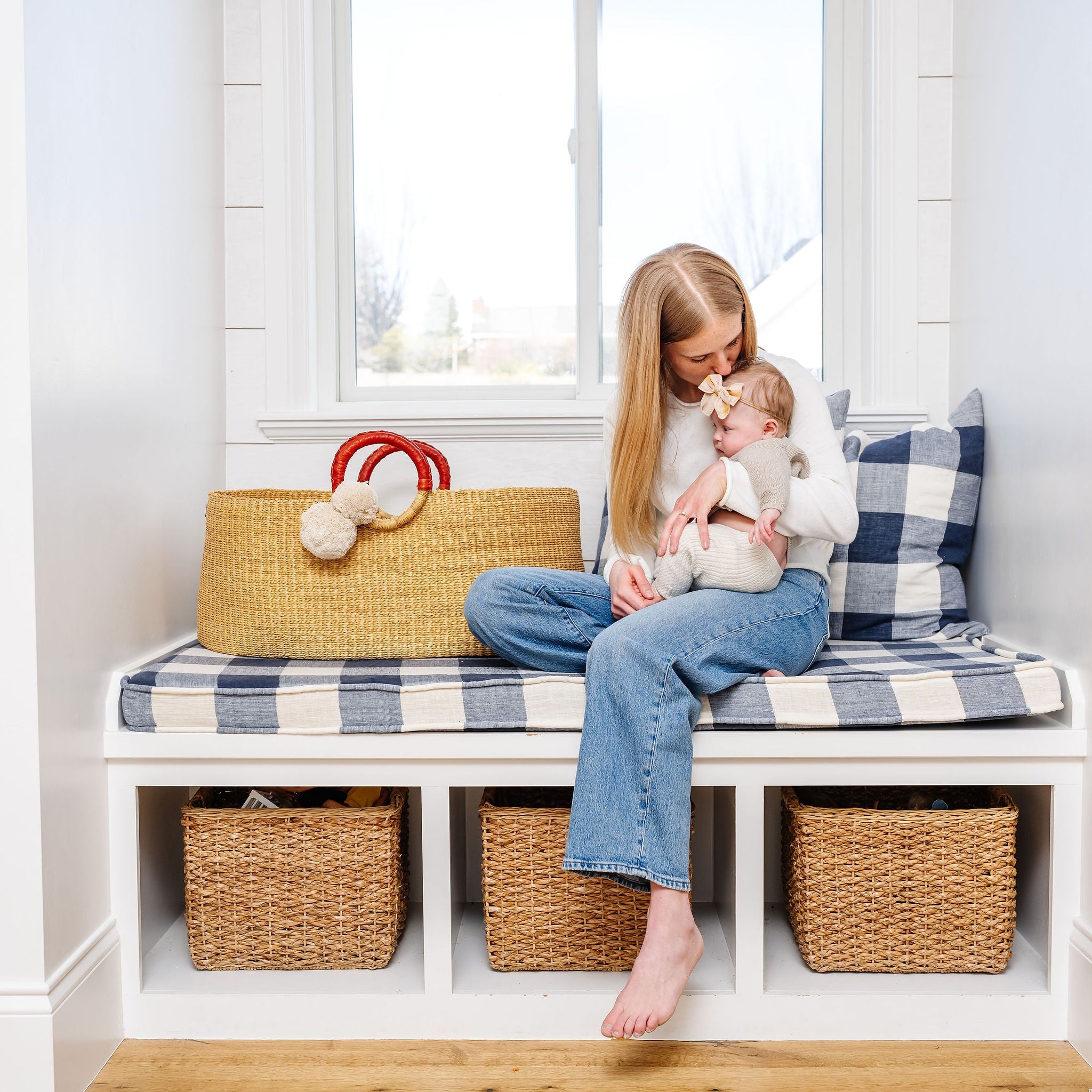 Woman sitting on a bench with a child, surrounded by storage baskets and a plaid pillow.