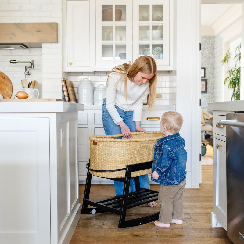 Woman and child in a kitchen with a baby bassinet.