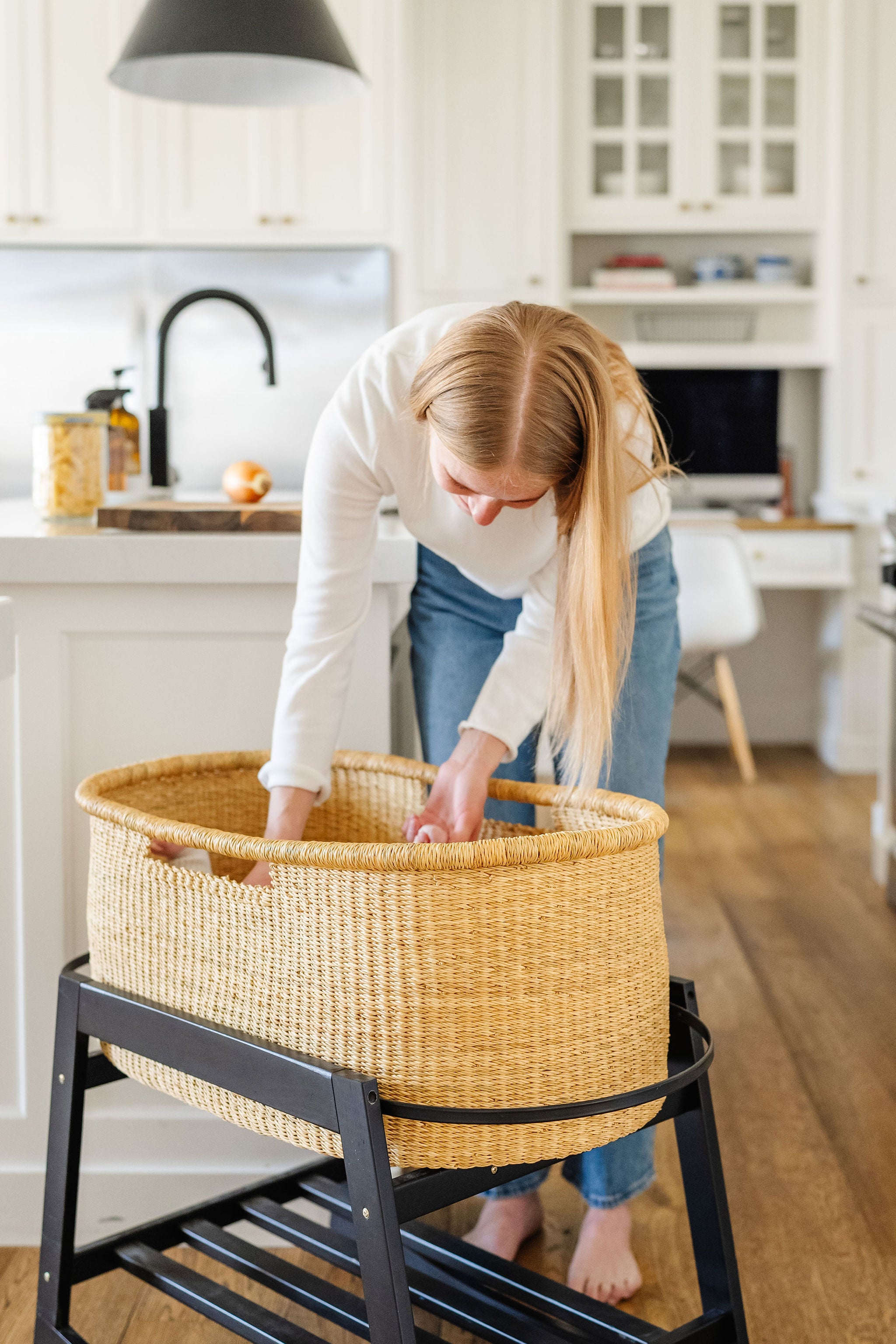 Woman moving a wicker baby crib in a kitchen.