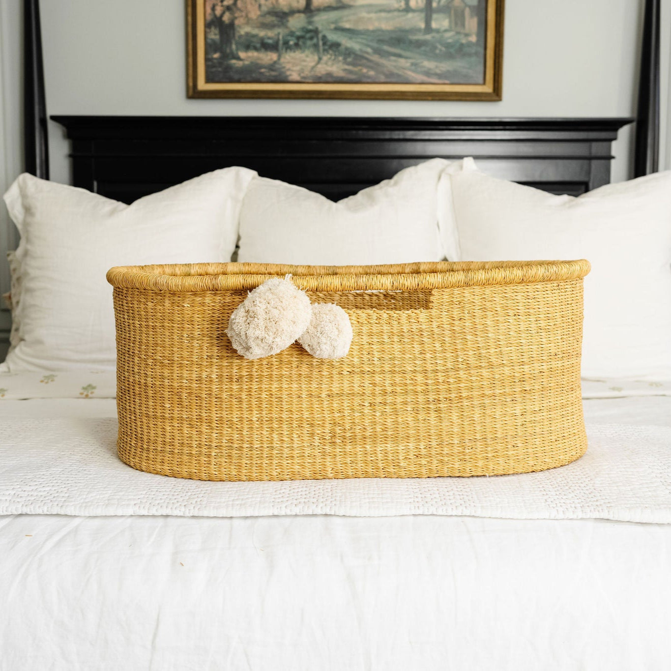 Wicker basket with decorative pom-poms on a bed in a bedroom setting.