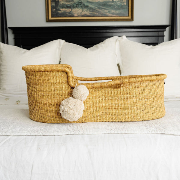 Woven basket with pom-poms on a bed in a bedroom setting